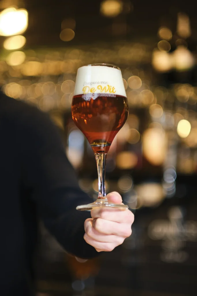 Hand houdt een glas robijnrood bier met witte schuimkraag voor de bar