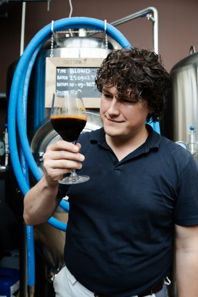 Brouwer beoordeelt een donker bier in een proefglas bij de gistank