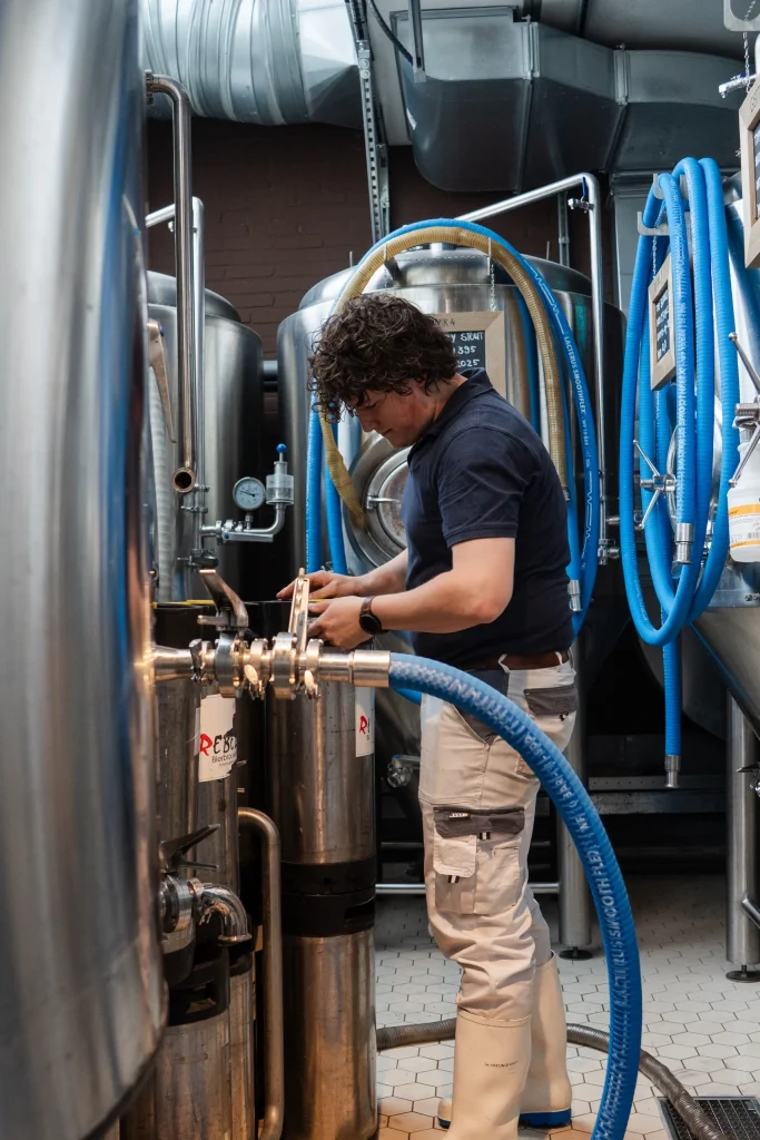 Brouwer sluit een slang aan op een tank in de brouwerij