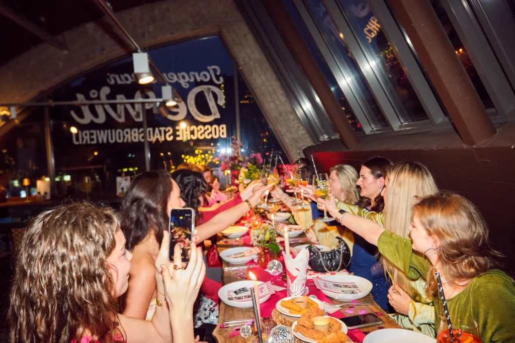 Feestelijk gedekte lange tafel waar een gezelschap samen proost