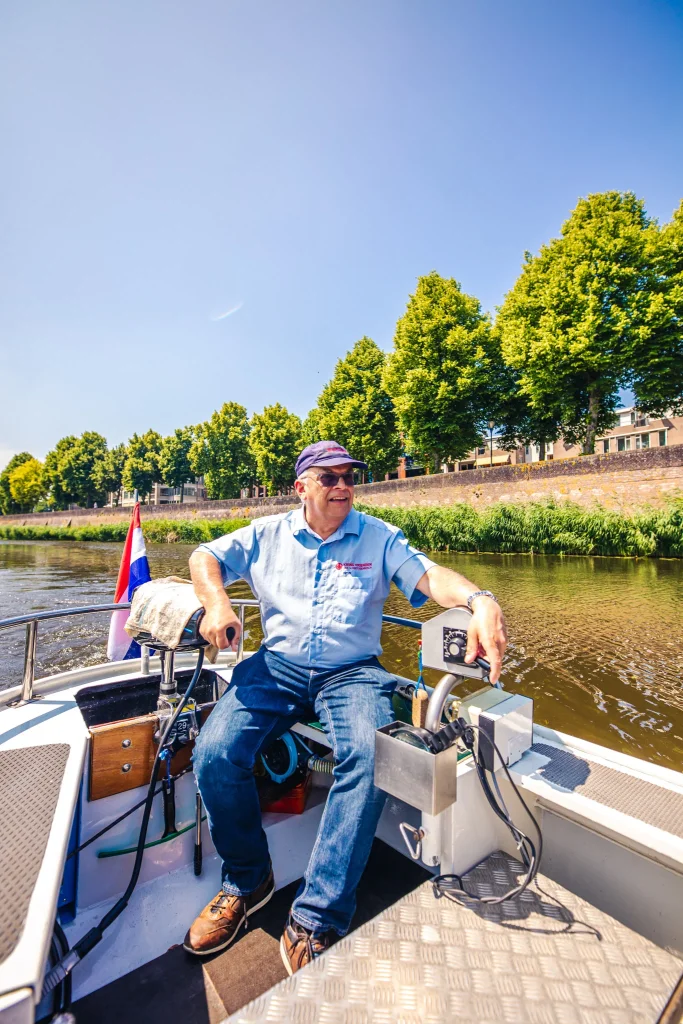 Schipper vaart een open rondvaartboot langs een begroeide kade